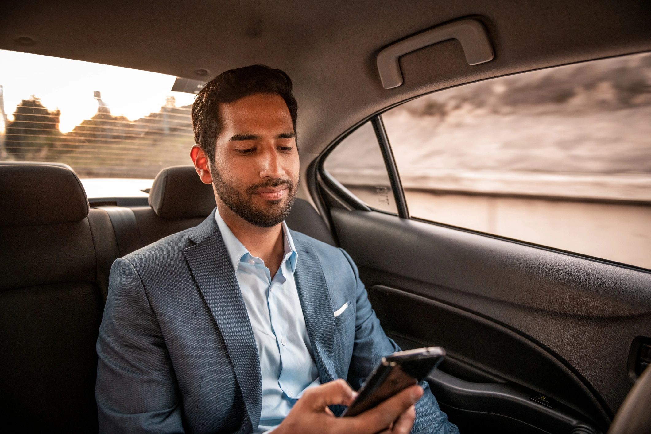 Business traveler riding in the back seat of a car using a phone